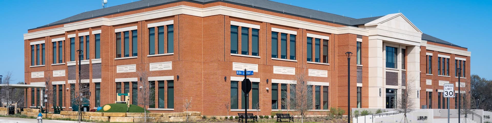 A large brick building with a central entrance, a speed limit sign of 30, and a clear blue sky.