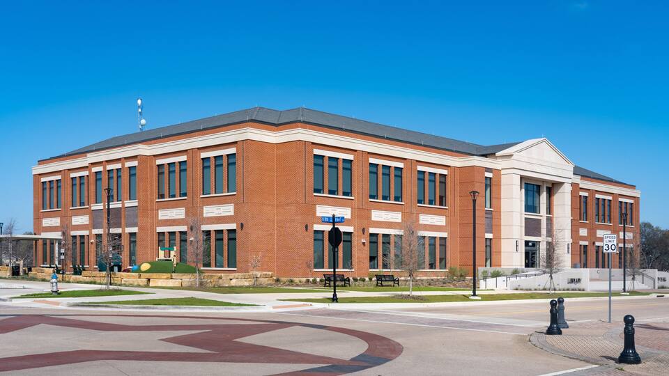 A large brick building with a central entrance, a speed limit sign of 30, and a clear blue sky.