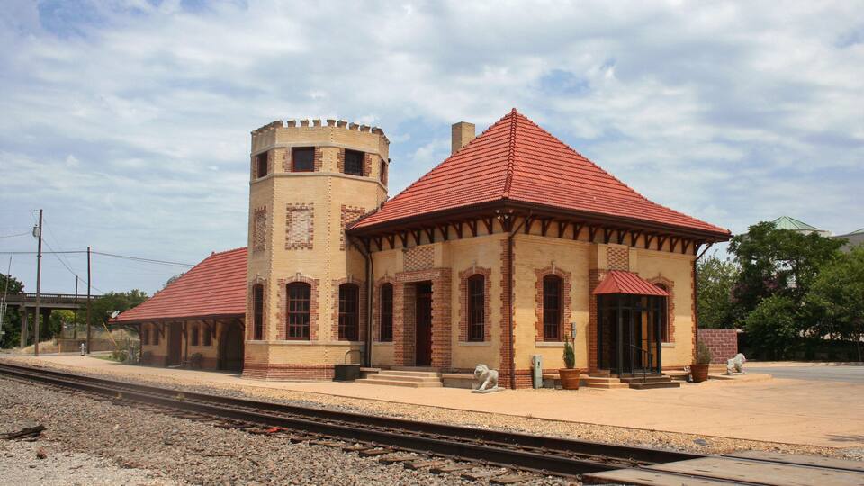 A historic train station with a tower and a red-roofed building.