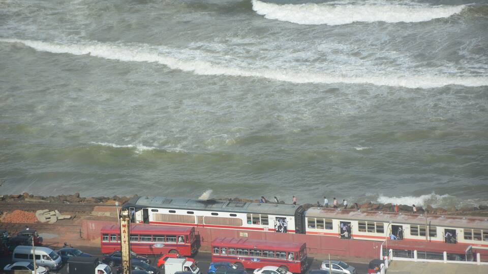 A coastal scene with a ferry, buses, and parked cars near the shore.