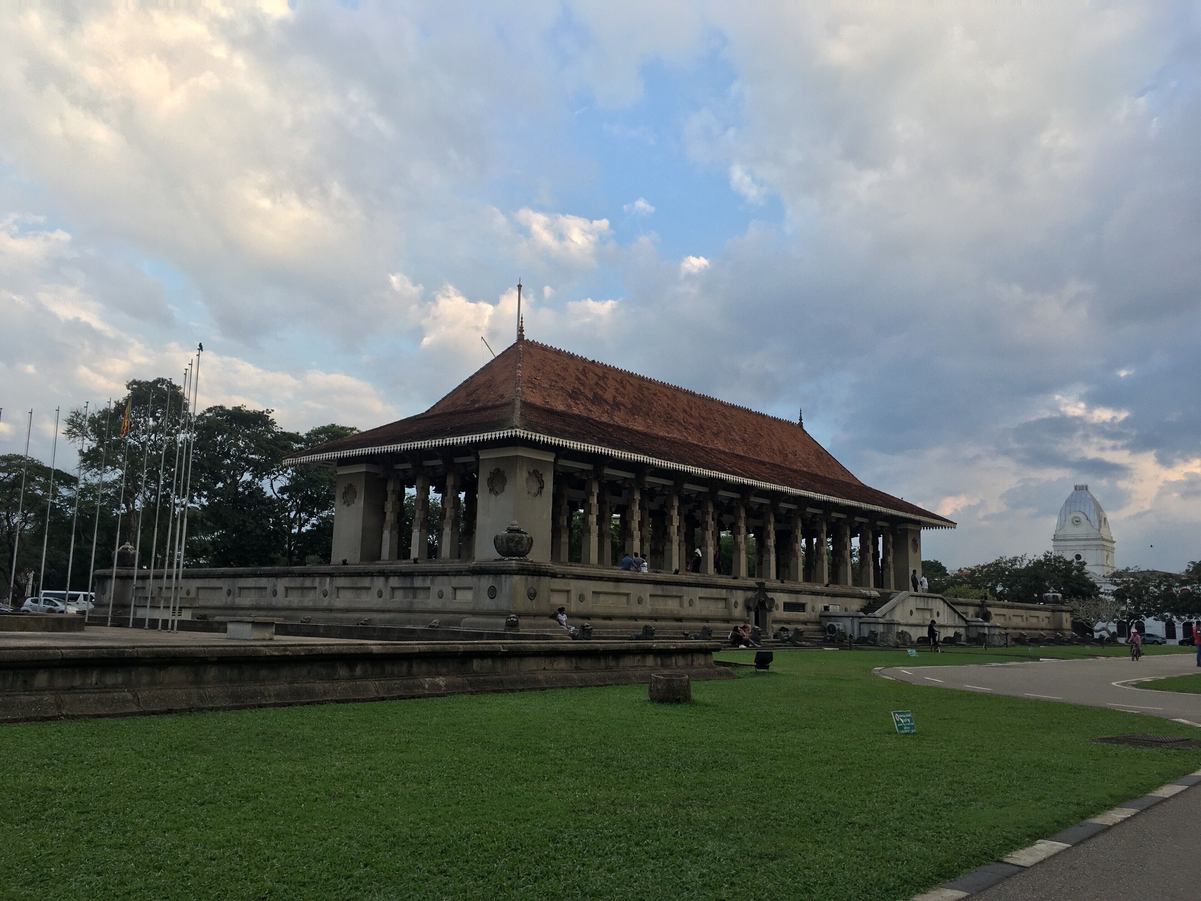 A historic building with a red-tiled roof and columns, surrounded by a well-maintained lawn and a large fountain.