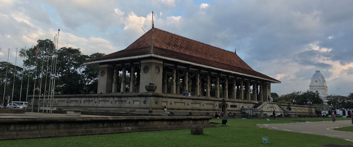 A historic building with a red-tiled roof and columns, surrounded by a well-maintained lawn and a large fountain.