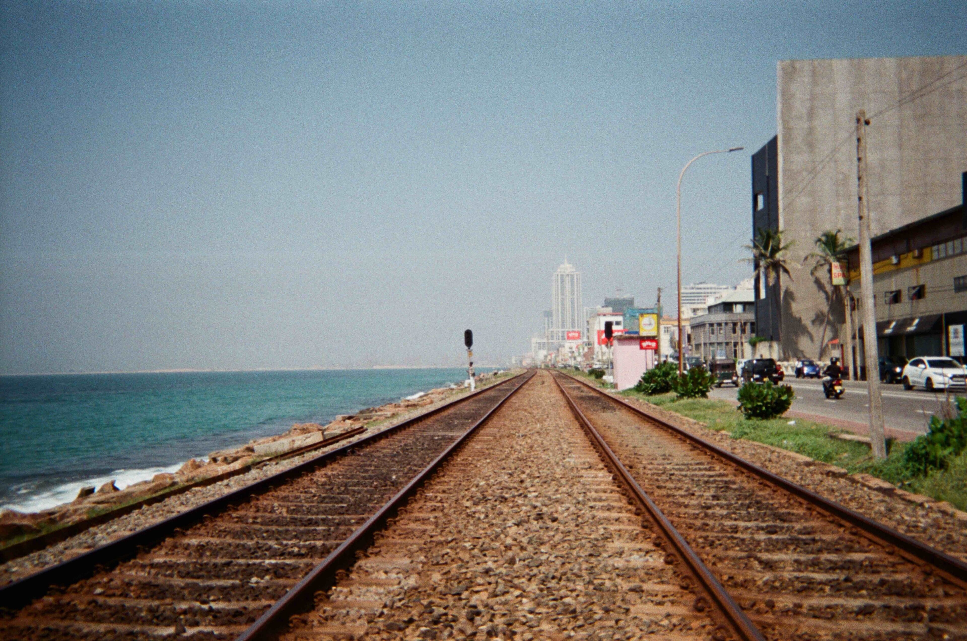 A railway track leading to a coastal city with buildings and palm trees.