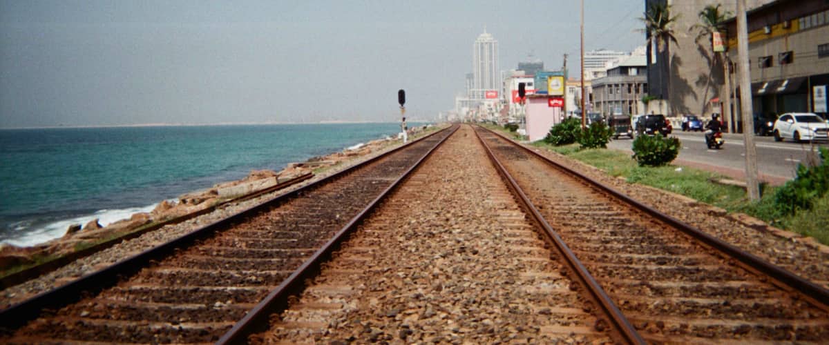 A railway track leading to a coastal city with buildings and palm trees.