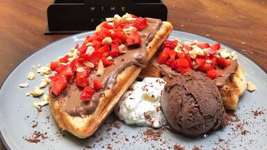 A plate of waffles topped with chocolate and strawberries, a scoop of ice cream, and a coffee cup on a table.