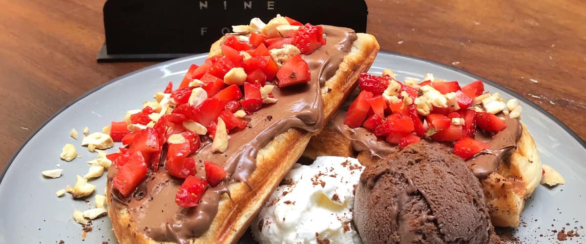 A plate of waffles topped with chocolate and strawberries, a scoop of ice cream, and a coffee cup on a table.