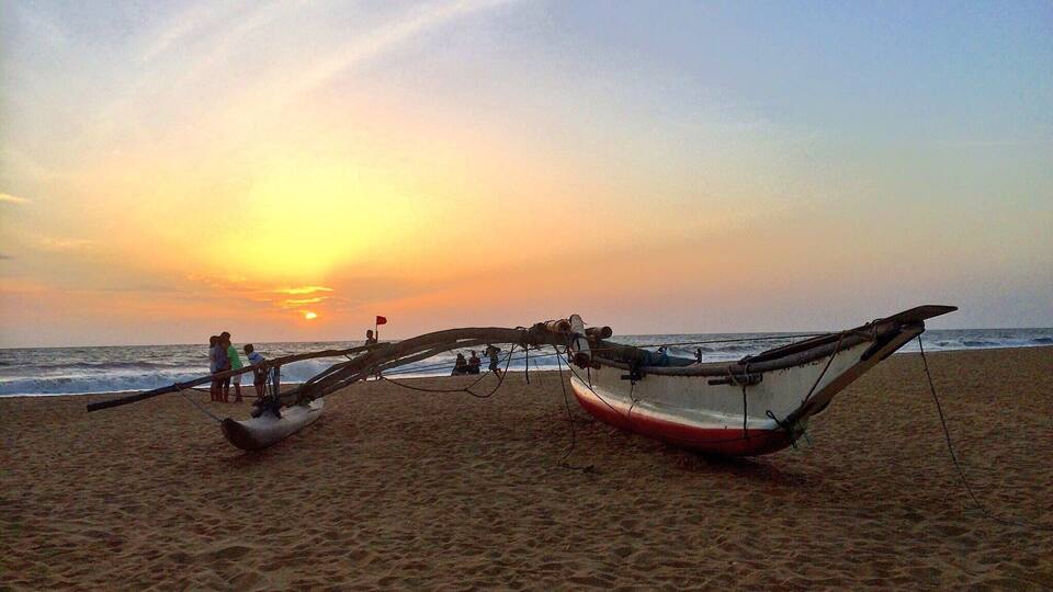 Dos barcos en una playa arenosa, con el océano al fondo y un atardecer en el cielo.
