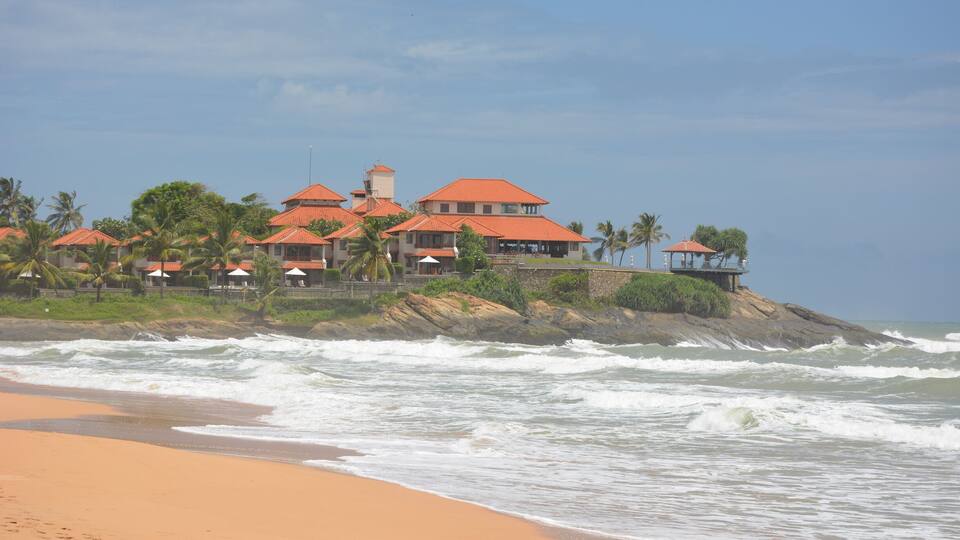 Una playa con una hilera de edificios de techo rojo y palmeras.