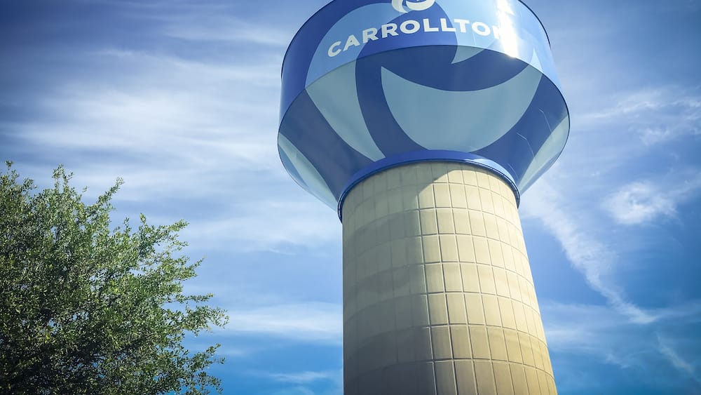 Huge, tall public water tower in Carrollton, Texas, USA against cloud blue sky and green trees. Close-up utility tank. Vintage tone