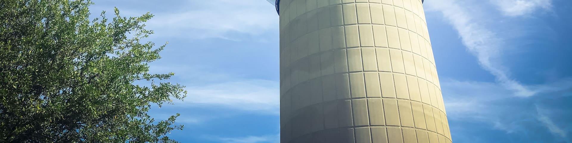 Huge, tall public water tower in Carrollton, Texas, USA against cloud blue sky and green trees. Close-up utility tank. Vintage tone
