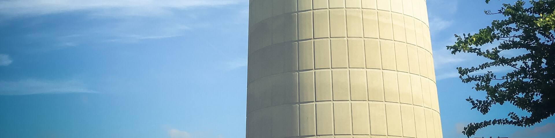 Huge, tall public water tower in Carrollton, Texas, USA against cloud blue sky and green trees. Close-up utility tank. Vintage tone