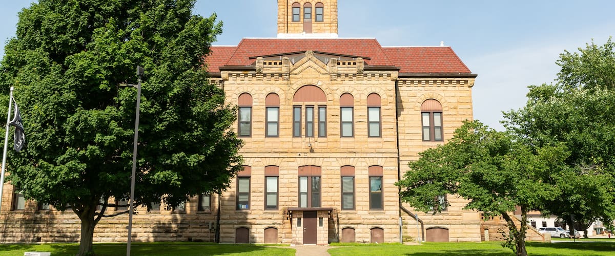 A historic stone building with a clock tower, surrounded by well-maintained lawns and trees.
