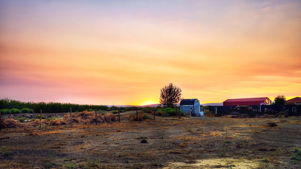 A rural landscape with a sunset, a barn, and a fence.
