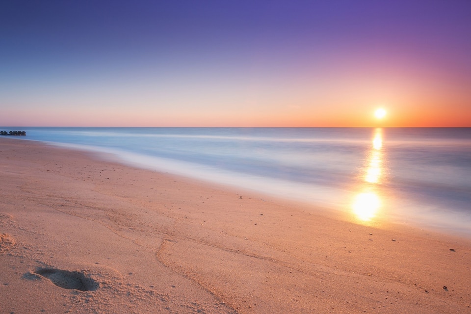 A beach with footprints leading to the water and a sunset in the background.