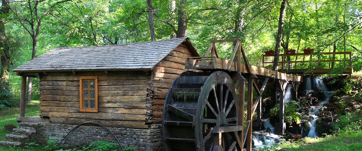 A wooden mill with a large water wheel and a wooden structure with a window.