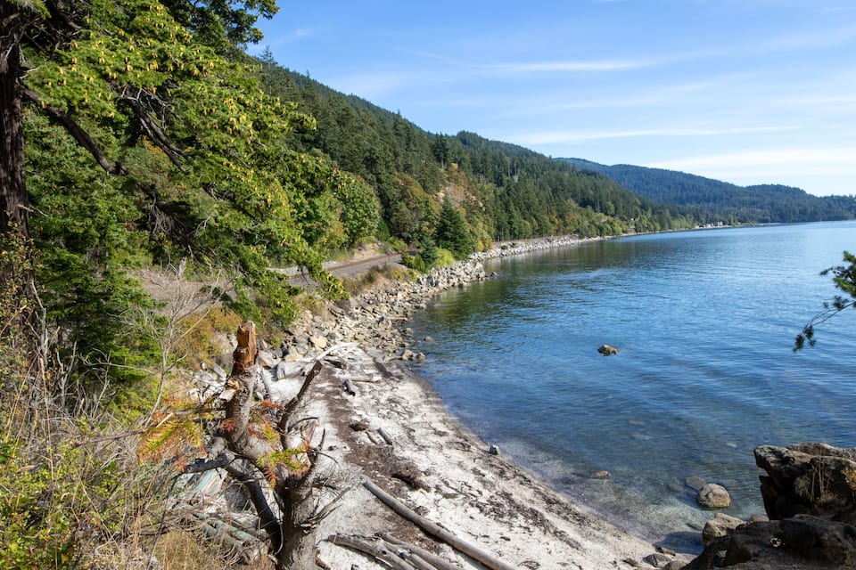 A clear lake with a rocky shoreline, surrounded by dense green forest and hills in the background.