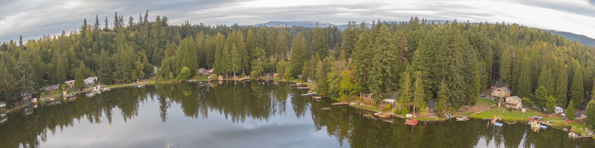 Un lago tranquilo rodeado de un bosque denso y casas.