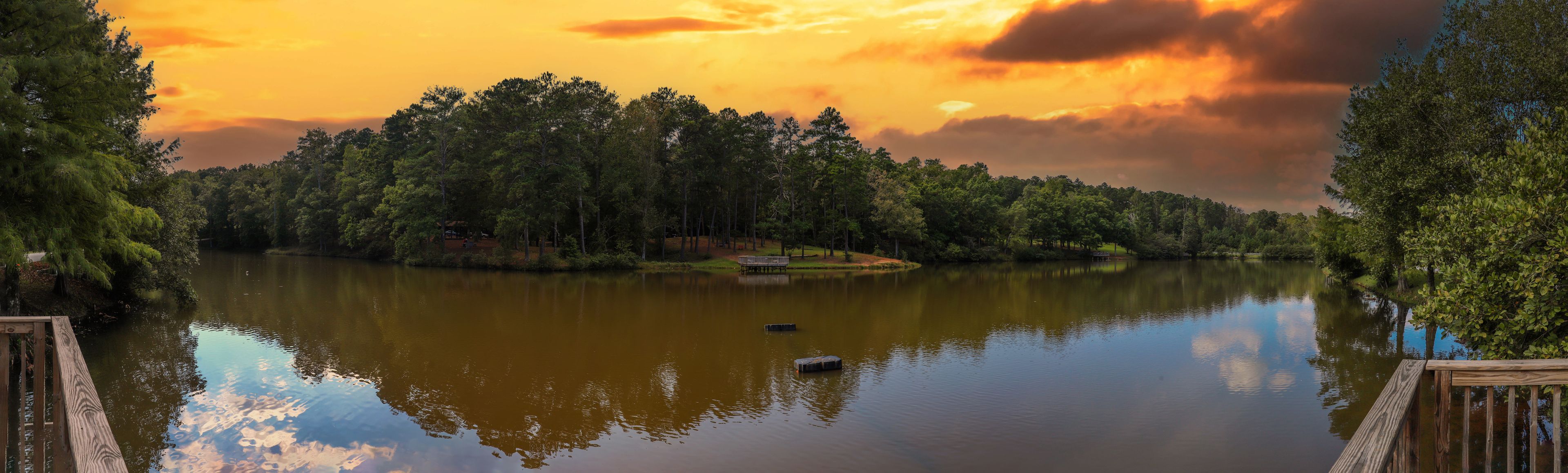 A calm lake surrounded by dense forest with a wooden dock on the left.
