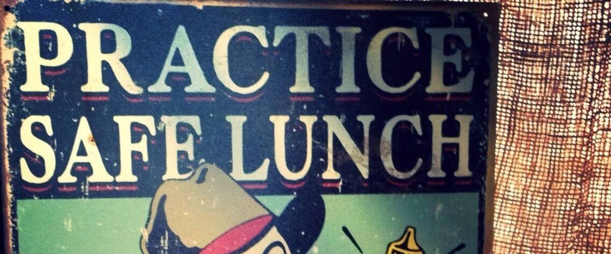 A vintage sign with a cartoon character holding a hot dog and a bottle of mustard, and a plush toy next to it.