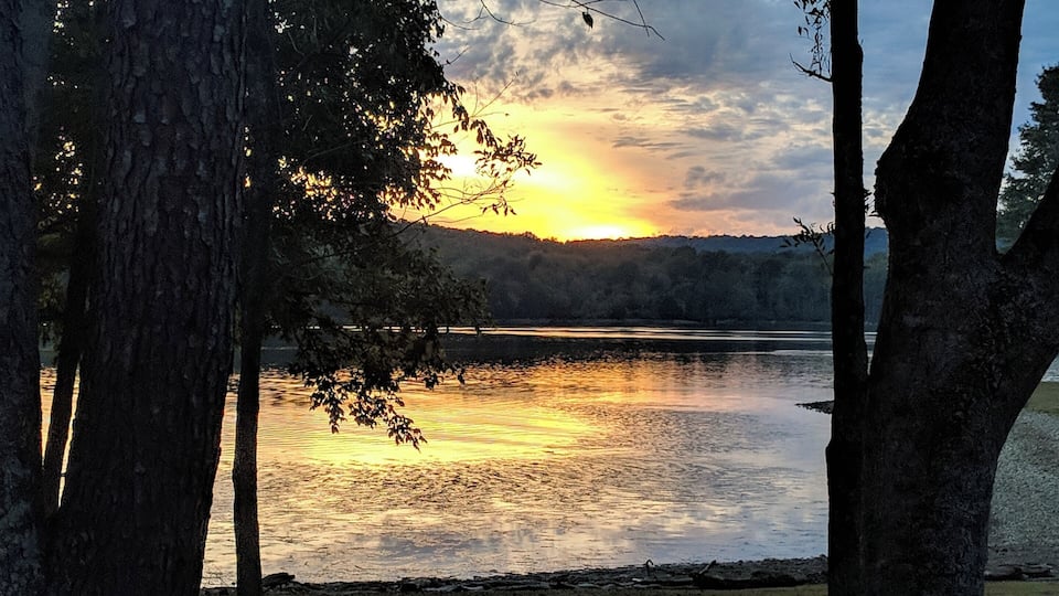 A sunset over a calm lake with trees in the foreground.