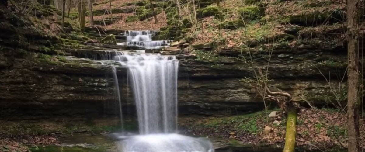 A waterfall cascading over layered rock formations in a forested area.