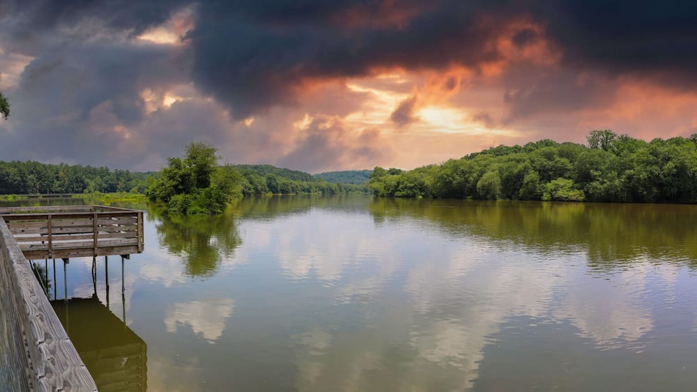 A wooden pier extending over a calm lake, surrounded by dense forest and under a dramatic sky.