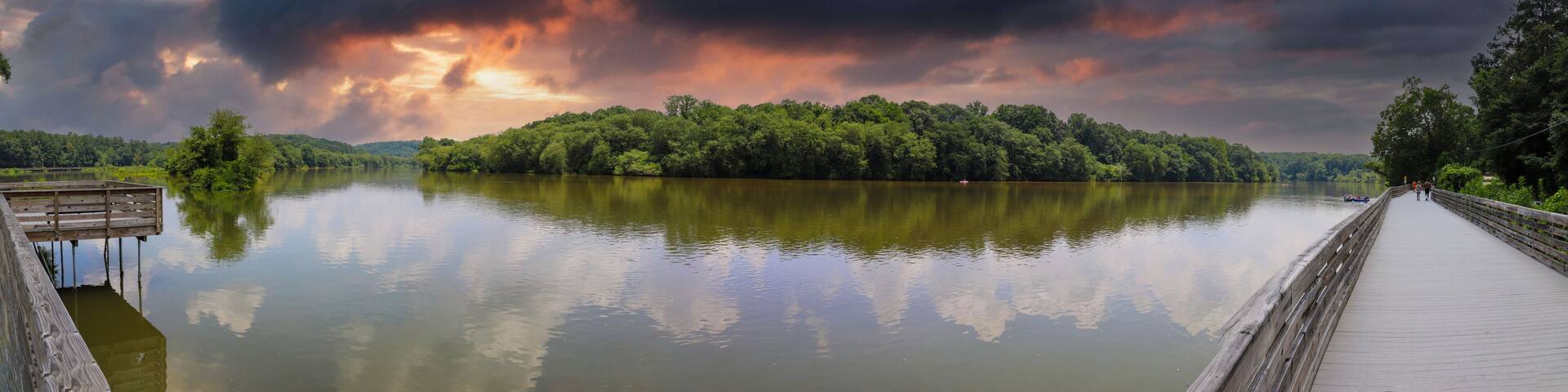 A wooden pier extending over a calm lake, surrounded by dense forest and under a dramatic sky.