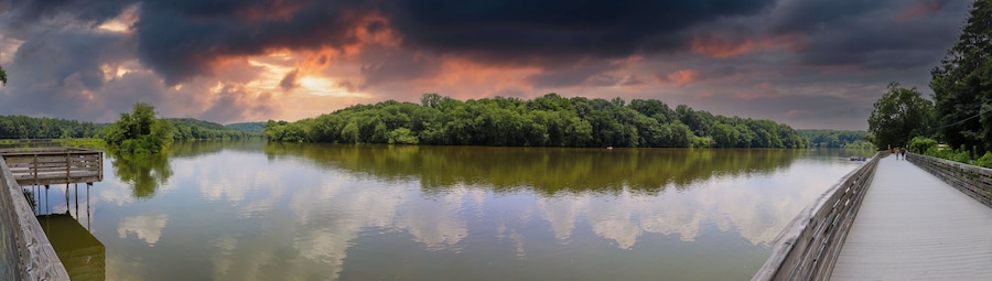 A wooden pier extending over a calm lake, surrounded by dense forest and under a dramatic sky.