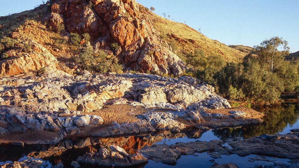 A rocky landscape with a large hill and a calm lake reflecting the scenery.