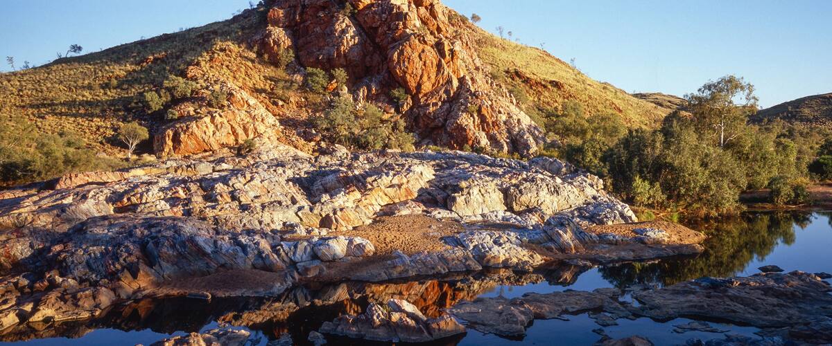 A rocky landscape with a large hill and a calm lake reflecting the scenery.