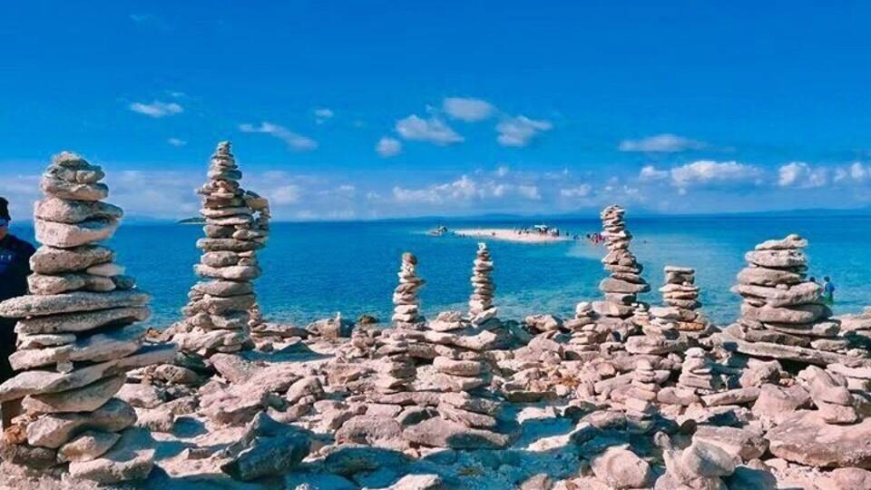 Stacks of rocks by the sea, clear blue sky, and distant boats.