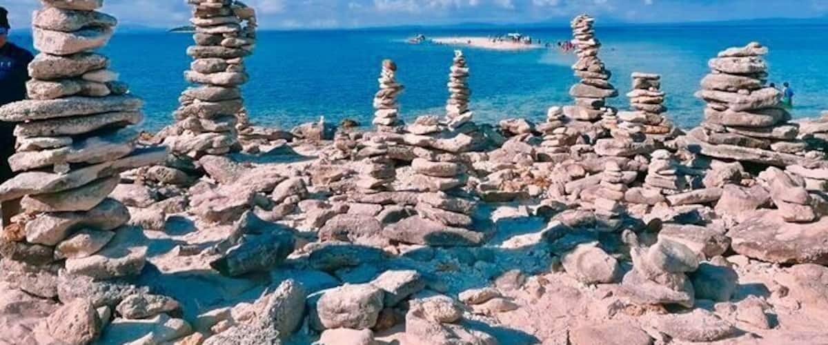 Stacks of rocks by the sea, clear blue sky, and distant boats.