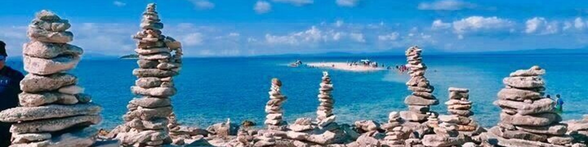 Stacks of rocks by the sea, clear blue sky, and distant boats.