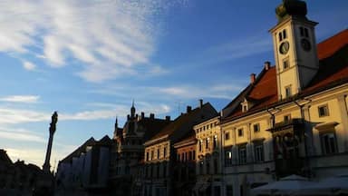 A historic town square with a prominent clock tower, traditional buildings, and a clear blue sky.