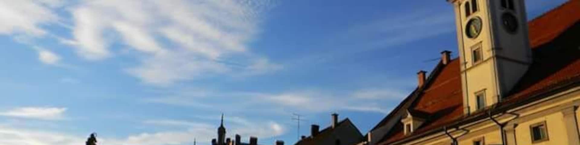Una plaza histórica con una imponente torre del reloj, edificios tradicionales y un cielo azul despejado.