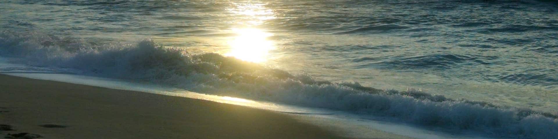 A beach with waves and a setting sun.