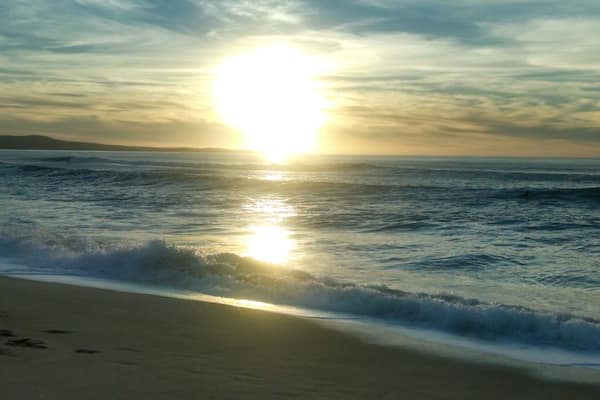 Une plage avec des vagues et un soleil couchant.