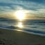 A beach with waves and a setting sun.