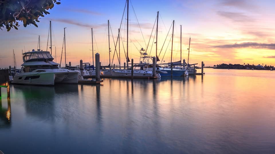 A marina at sunset with boats docked and a wooden pier.
