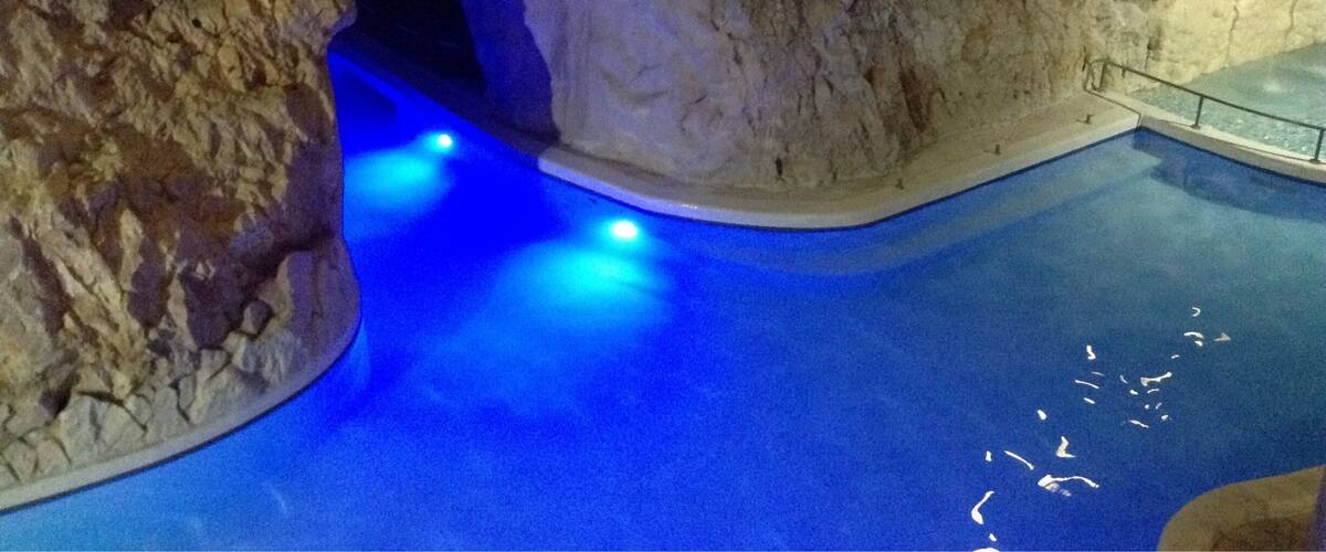 A pool with blue lighting and a rocky cave-like structure.