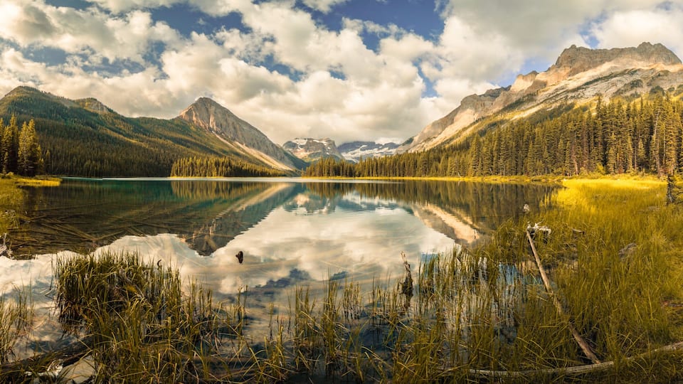 A mountain lake with reflections, surrounded by dense forests and mountains.