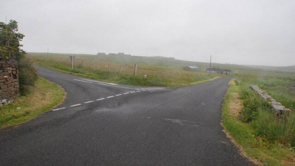 A rural road with a sharp bend, stone walls, and open fields.