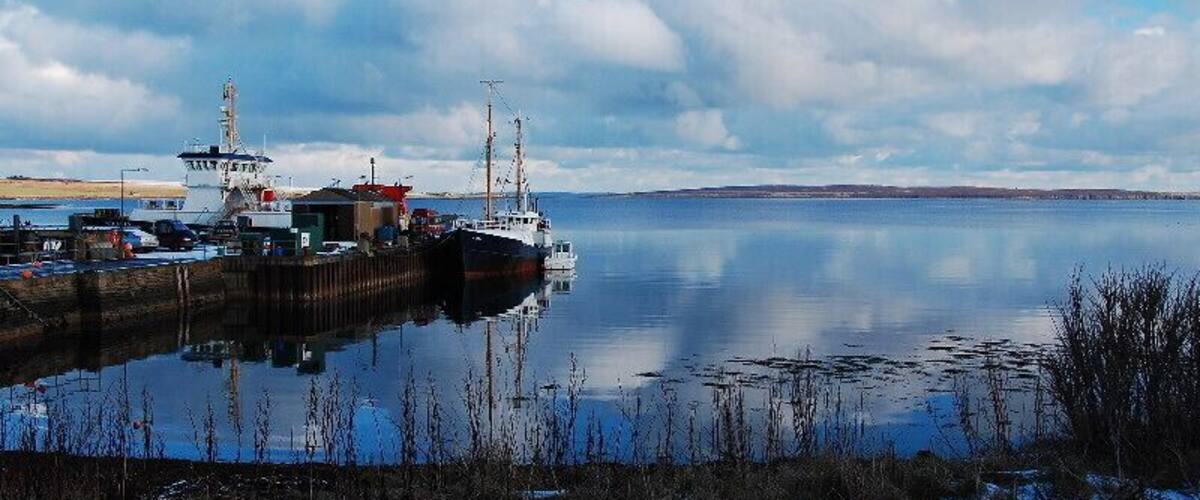 A calm harbor with a docked ship, a lighthouse, and a snow-covered shoreline.