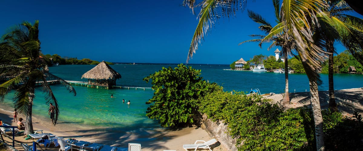 A tropical beach with clear turquoise water, palm trees, and a thatched-roof hut.