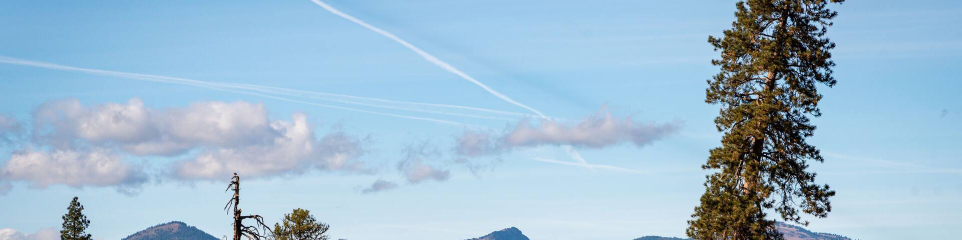 Un paysage montagneux, avec un ciel dégagé, quelques nuages épars et une petite cabane au premier plan.