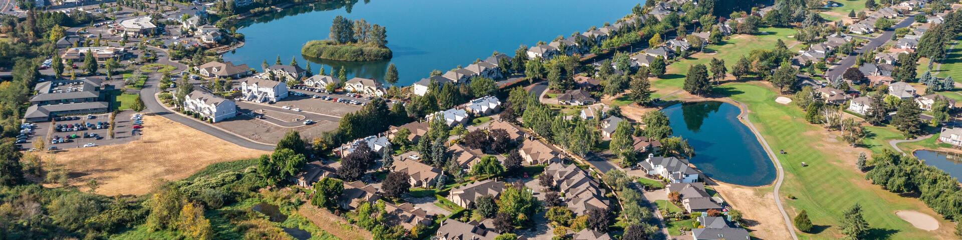 An aerial view of a lakeside residential area with houses, a golf course, and a large body of water.