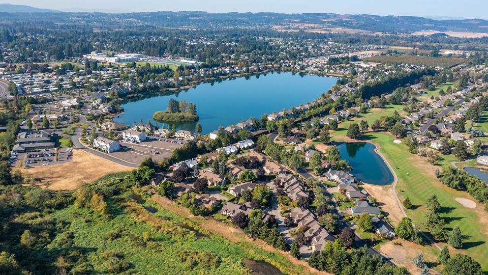 An aerial view of a lakeside residential area with houses, a golf course, and a large body of water.