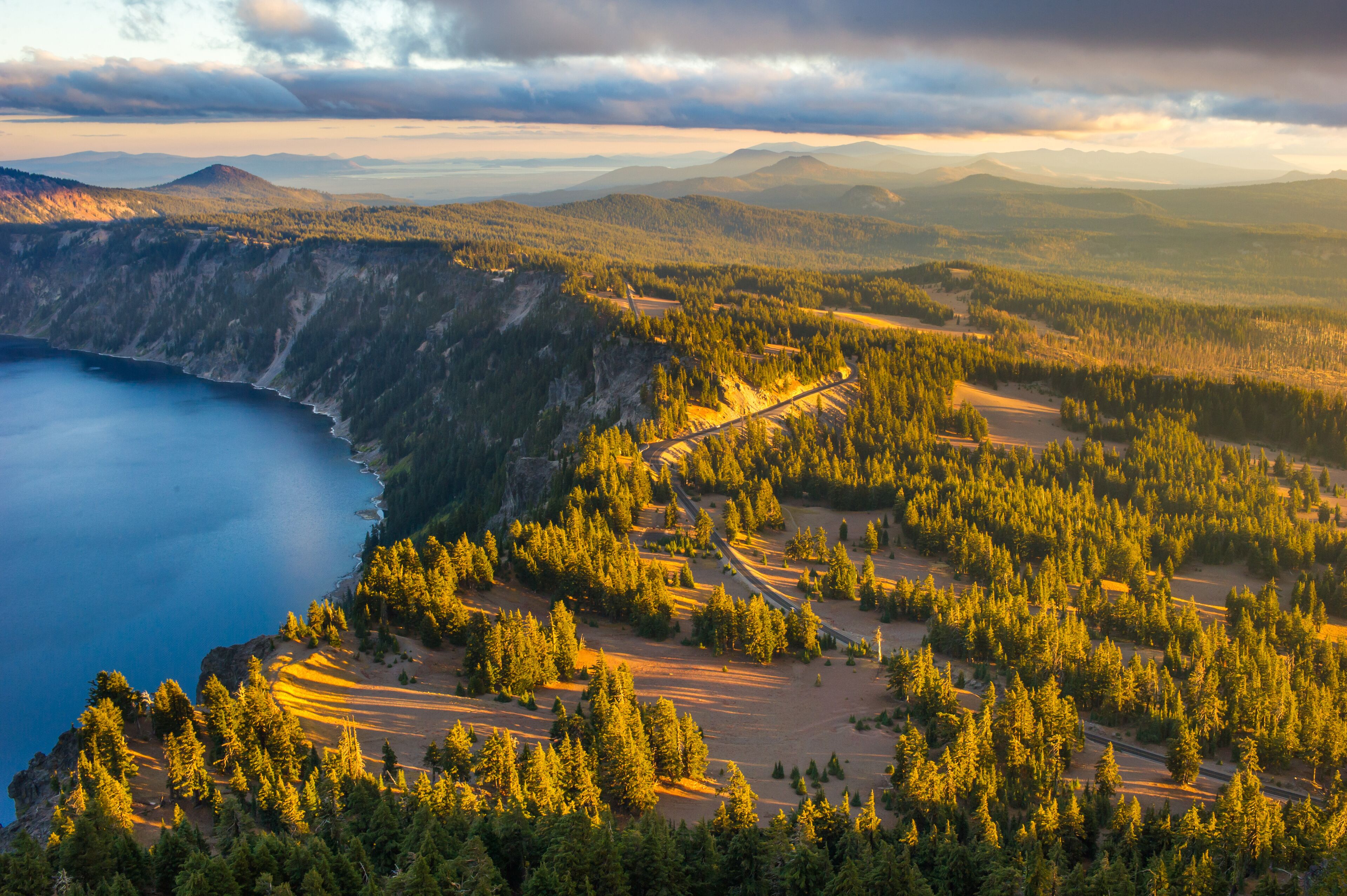 A mountainous landscape with a forested area, a clear blue lake, and a winding road.