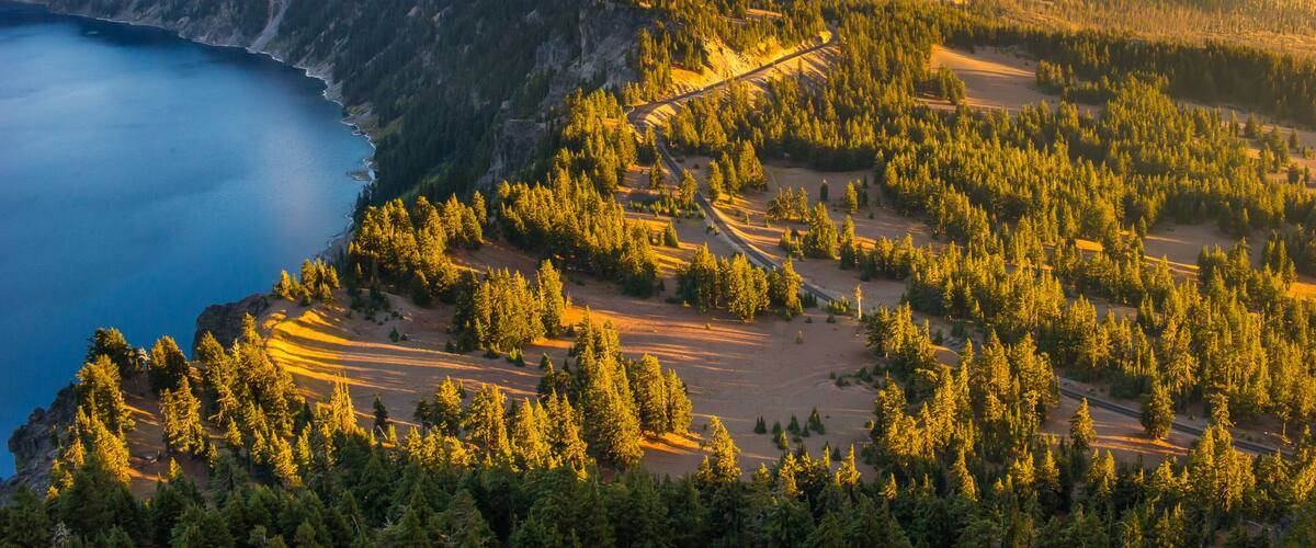 A mountainous landscape with a forested area, a clear blue lake, and a winding road.