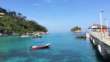 Paisaje costero con aguas turquesas cristalinas, un muelle y barcos.
